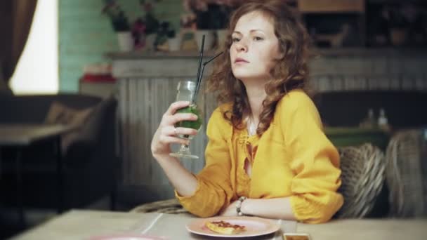 Молодая женщина пьет коктейль в кафе-баре — стоковое видео