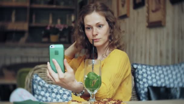 Μια νεαρή γυναίκα ένα κοκτέιλ τα ποτά στο καφέ-μπαρ και χρησιμοποιεί ένα τηλέφωνο — Αρχείο Βίντεο