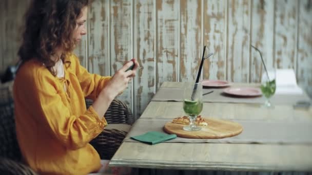 Genç kadın bir kafe barda bir smartphone cep telefonu ile bir pasta lazım — Stok video