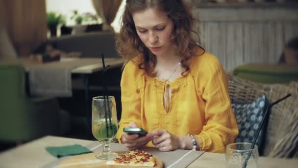 Une jeune femme boit un cocktail dans un café-bar et utilise un téléphone — Video