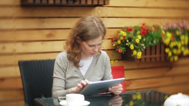 Mujer joven utiliza una tableta y teléfono, bebe té en un bar cafetería — Vídeos de Stock