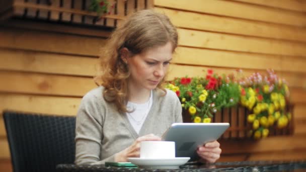 Mujer joven utiliza una tableta y teléfono, bebe té en un bar cafetería — Vídeos de Stock