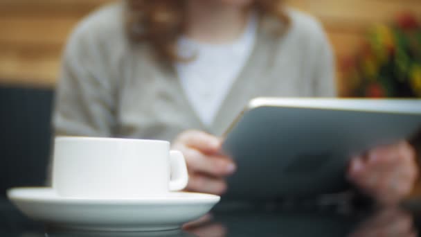 Une jeune femme utilise une tablette et un téléphone, boit du thé dans un café-bar — Video