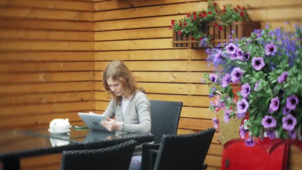 Mujer joven utiliza una tableta y teléfono, bebe té en un bar cafetería — Vídeos de Stock