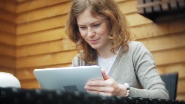 Giovane donna utilizza un tablet e telefono, beve il tè in un bar — Video Stock