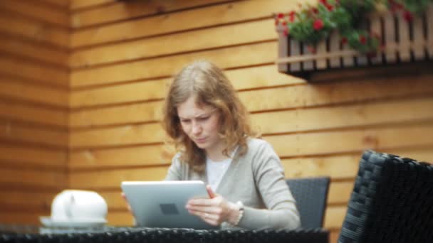 Mujer joven utiliza una tableta y teléfono, bebe té en un bar cafetería — Vídeos de Stock