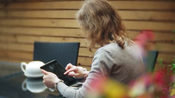 Молодая женщина пользуется планшетом и телефоном, пьет чай в кафе-баре — стоковое видео