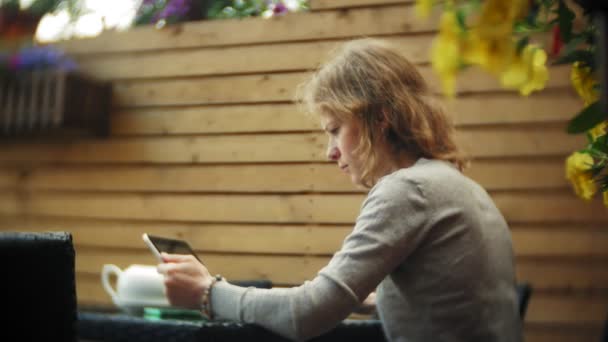 Mladá žena používá tablet a telefon, pije čaj v café bar — Stock video