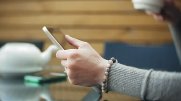 Mujer joven utiliza una tableta y teléfono, bebe té en un bar cafetería — Vídeo de stock