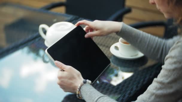 Giovane donna utilizza un tablet e telefono, beve il tè in un bar — Video Stock