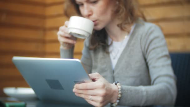 Giovane donna utilizza un tablet e telefono, beve il tè in un bar — Video Stock