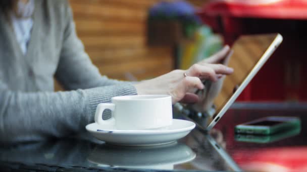 Ung kvinna använder en surfplatta och telefon, dricker te i en cafébar — Stockvideo