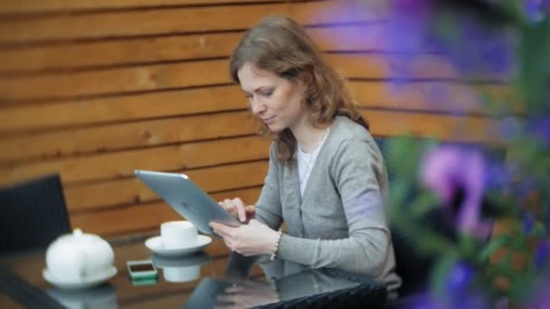 Молода жінка використовує планшет і телефон, п'є чай в кафе-барі — стокове відео