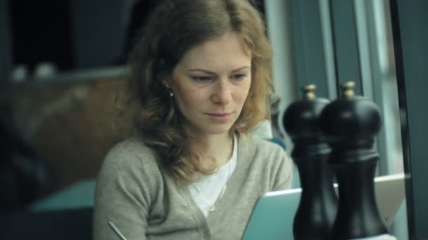 Une jeune femme utilise une tablette et un téléphone, boit du thé dans un café-bar — Video