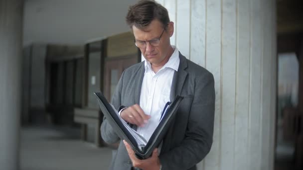 Молодой, уважаемый бизнесмен, отправленный в офисное здание. В руках он держит портфель, просматривает документы. . — стоковое видео