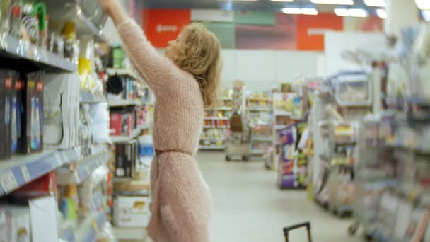 Mujer joven se para cerca de la estantería del supermercado y selecciona los productos — Vídeo de stock