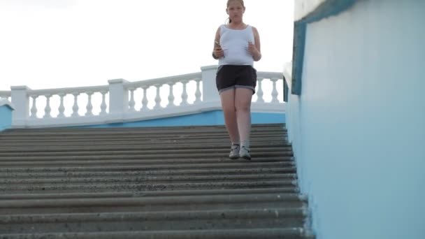 Jeune fille grosse courir dans les escaliers, perdre du poids, écouter de la musique dans un casque concept de mode de vie sain super ralenti — Video