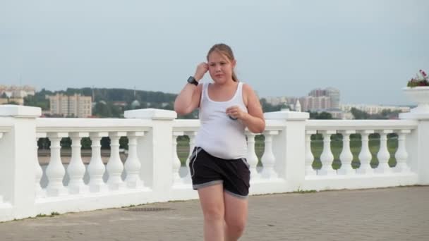 Menina gorda jovem correndo, derramando peso, ouvindo música em fones de ouvido conceito de estilo de vida saudável — Vídeo de Stock