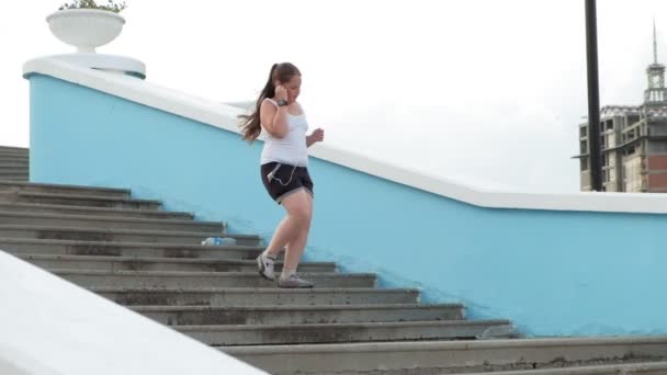 Ung fett flicka kör nedför trappor, kasta vikt, lyssna på musik i hörlurar begreppet hälsosam livsstil super slow motion — Stockvideo