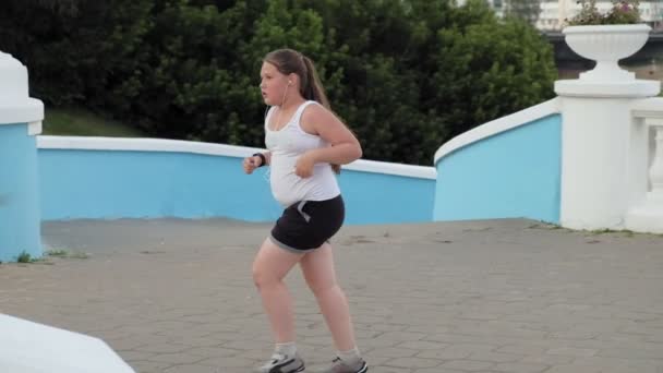Jonge vet meisje rennen trappen, vergieten gewicht, luisteren naar muziek in hoofdtelefoons concept van gezonde levensstijl super slow motion — Stockvideo