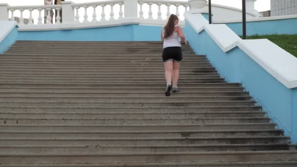 Niña gorda corriendo escaleras abajo, perdiendo peso, escuchando música en los auriculares concepto de estilo de vida saludable super cámara lenta — Vídeos de Stock