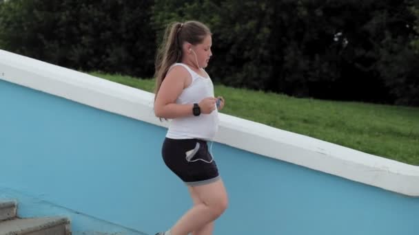 Junges dickes Mädchen, das Treppen rennt, Gewicht abnimmt, über Kopfhörer Musik hört, Konzept eines gesunden Lebensstils Super-Zeitlupe — Stockvideo