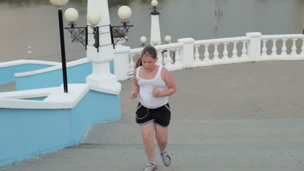 Молодая толстая девушка бежит вниз по лестнице, сбрасывая вес, слушая музыку в наушниках концепции здорового образа жизни супер медленное движение — стоковое видео