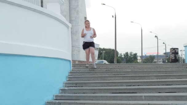 Jonge vet meisje rennen trappen, vergieten gewicht, luisteren naar muziek in hoofdtelefoons concept van gezonde levensstijl super slow motion — Stockvideo