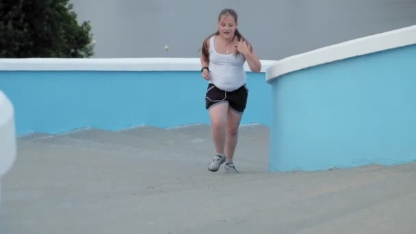 Jeune fille grosse courir dans les escaliers, perdre du poids, écouter de la musique dans un casque concept de mode de vie sain super ralenti — Video