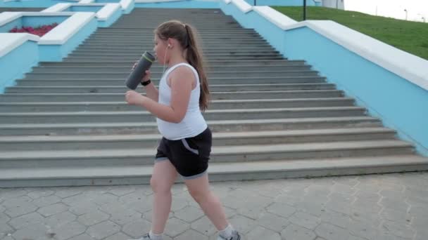 Niña gorda corriendo escaleras abajo, perdiendo peso, escuchando música en los auriculares concepto de estilo de vida saludable super cámara lenta — Vídeos de Stock