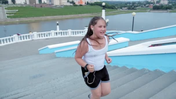 年轻的胖女孩跑下楼, 脱落重量, 听音乐在耳机健康生活方式的概念超慢动作 — 图库视频影像