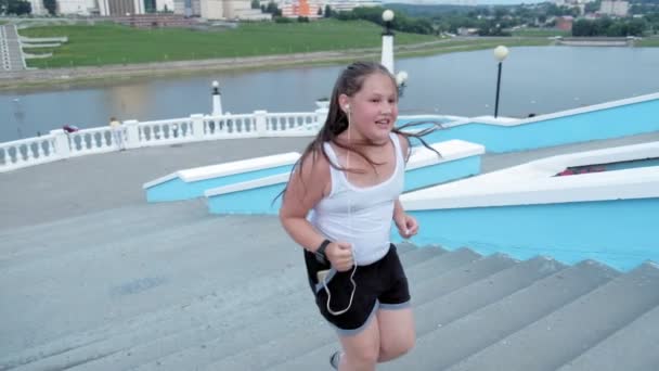 Niña gorda corriendo escaleras abajo, perdiendo peso, escuchando música en los auriculares concepto de estilo de vida saludable super cámara lenta — Vídeos de Stock