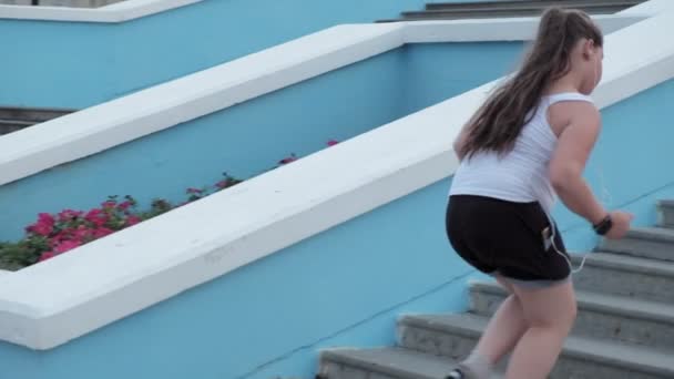 Giovane ragazza grassa correre giù per le scale, perdere peso, ascoltare musica in cuffie concetto di stile di vita sano super slow motion — Video Stock