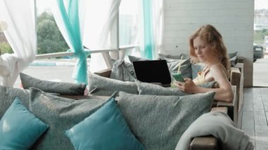 Genç iş kadını masada Mojito kokteyl oturma ve çekici notlar not defterinde içme. Bir dizüstü bilgisayar, akıllı telefon olacak. Öğretim öğrencileri online. Blogger.