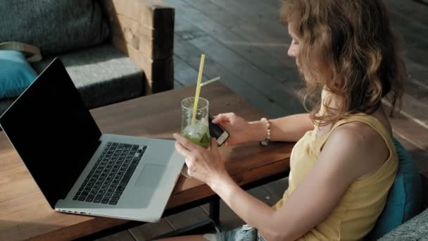 Joven mujer de negocios bebiendo cóctel mojito sentada en la mesa y tomando notas en el cuaderno. Enseñando a los estudiantes en línea. Blogger . — Vídeo de stock