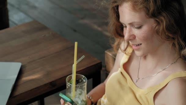 Young business woman drinking mojito cocktail sitting at table and taking notes in notebook.On is a laptop, smartphone. Teaching students online. Blogger. — Stock Video