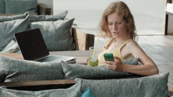 Jonge zakenvrouw drinken mojito cocktail vergadering aan tafel en het maken van notities in een notitieblok. Een laptop, smartphone is. Onderwijs studenten online. Blogger. — Stockvideo