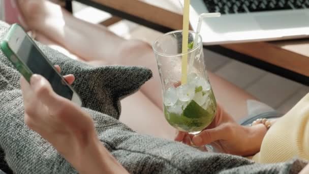 Junge Geschäftsfrau trinkt Mojito-Cocktail sitzt am Tisch und macht Notizen in Notizbuch.on ist ein Laptop, Smartphone. Studenten online unterrichten. Blogger. — Stockvideo