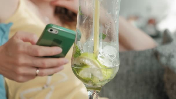 Ung affärskvinna dricka mojito cocktail sittande vid bord och anteckningar i anteckningsboken. Vidare är en laptop, smartphone. Lära elever online. Blogger. — Stockvideo