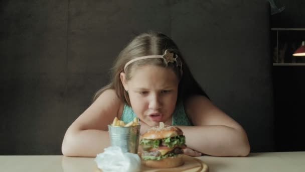 Dik meisje gretig eten van een hamburger, concept van een gezond dieet — Stockvideo