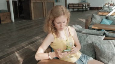Genç iş kadını masada Mojito kokteyl oturma ve çekici notlar not defterinde içme. Bir dizüstü bilgisayar, akıllı telefon olacak. Öğretim öğrencileri online. Blogger.
