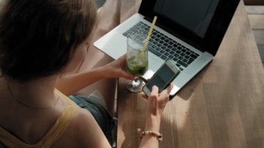 Genç iş kadını masada Mojito kokteyl oturma ve çekici notlar not defterinde içme. Bir dizüstü bilgisayar, akıllı telefon olacak. Öğretim öğrencileri online. Blogger.