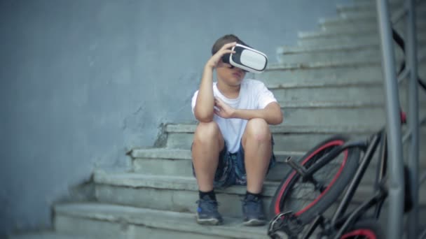 The boy is sitting on the ladder in virtual glasses, next to the bicycle BMX — Stock Video