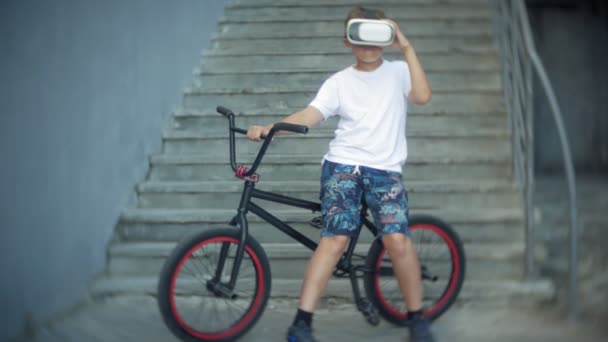 Το αγόρι κάθεται στη σκάλα στην εικονική γυαλιά, δίπλα από το ποδήλατο Bmx — Αρχείο Βίντεο