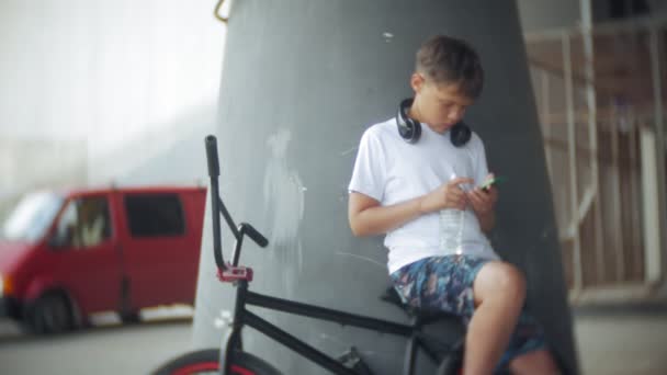 Pojken sitter på en Bmx-cykel och lyssnar på musik från en smartphone — Stockvideo
