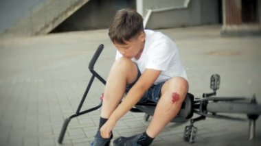 Genç bir çocuk bir parkta bir bisikletten düştükten sonra oturur, onun diz ağrısı yatıştırır, tehlikeli Bisiklete binmek.