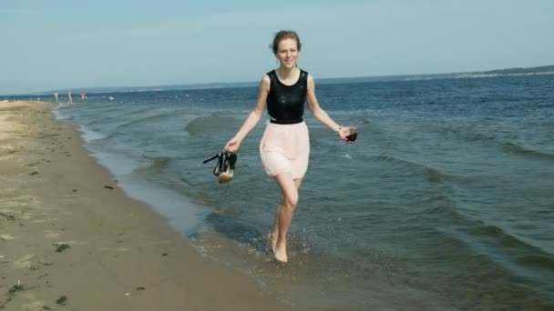 Giovane donna bionda in un bellissimo vestito godendo di un bicchiere di vino rosa sulla spiaggia vicino al mare, super slow motion — Video Stock