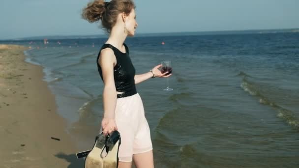 Joven mujer rubia en un hermoso vestido disfrutando de una copa de vino rosa en la playa cerca del mar, super cámara lenta — Vídeo de stock