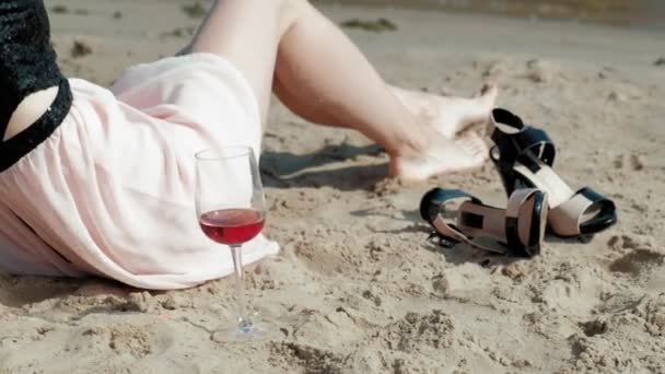 Jonge blonde vrouw in een mooie jurk, genieten van een glas roze wijn op het strand in de buurt van de zee, super slow motion — Stockvideo