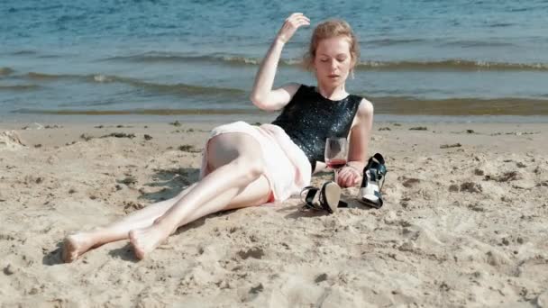 Junge blonde Frau in einem schönen Kleid genießt ein Glas rosa Wein am Strand in der Nähe des Meeres, Super-Zeitlupe — Stockvideo